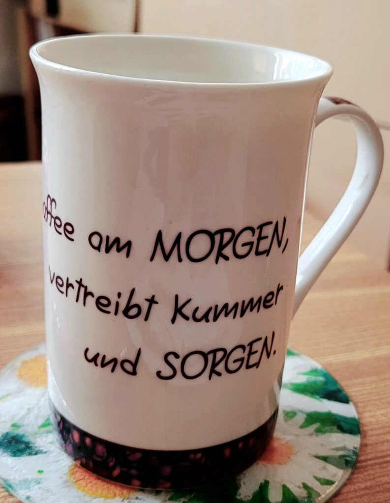 leere Tasse mit Spruch auf einem blumigen Untersetzer